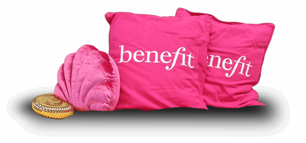Foto: Zwei rosafarbene Kissen mit der Aufschrift "benefit" und weitere Accessoires.
