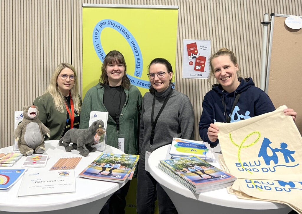 Foto von Lisa Radtke (rechts) zusammen mit drei jungen Frauen, die um zwei Tische mit Infomaterial zu Balu und Du herum stehen.