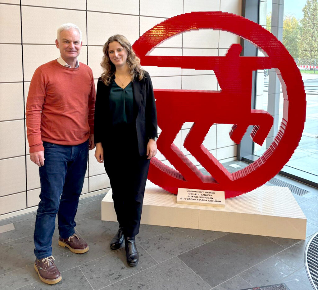 Foto: Nadine Holste (rechts) und Dr. Domink Esch (links) vor einem 3D-Logo von ROSSMANN.